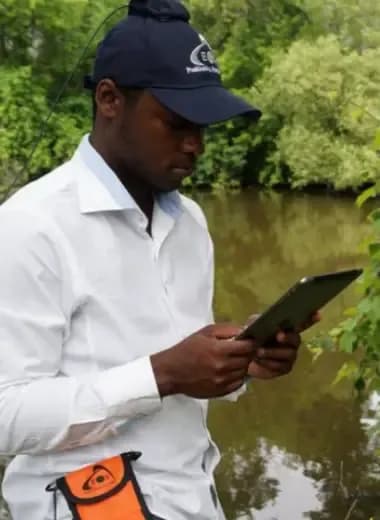 Surveyor collecting environmental data on a riverbank with a tablet
